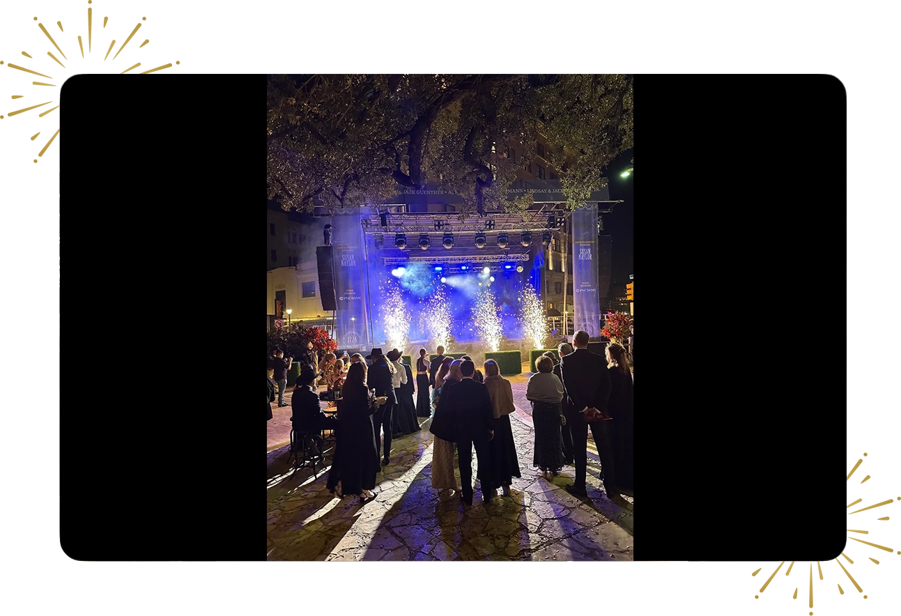 A crowd of people standing around in front of an outdoor stage.